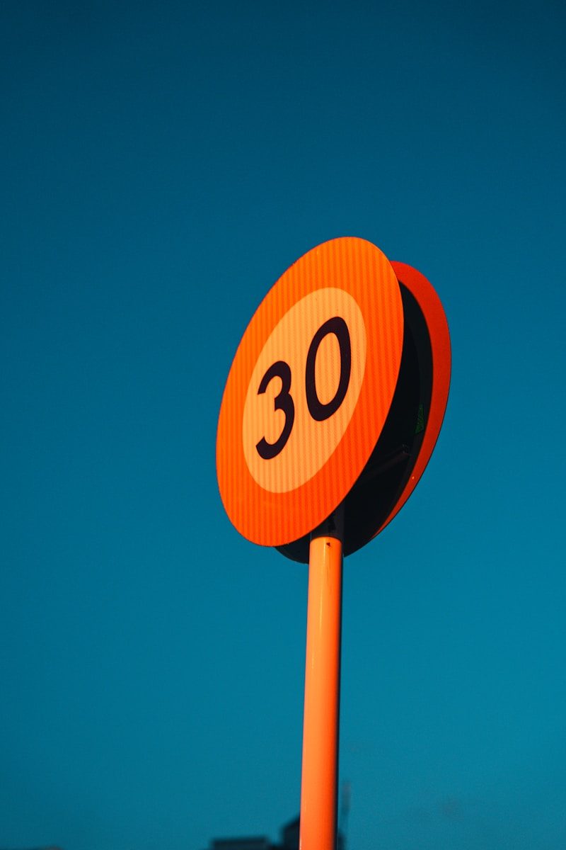 Orange speed limit sign showing 30 against blue sky.